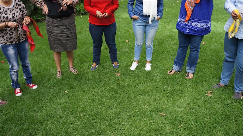Esto es una imagen. En la imagen se muestra un pasto verde y sobre él los pies de varias personas formando un medio círculo. No vemos las caras de estas personas. 